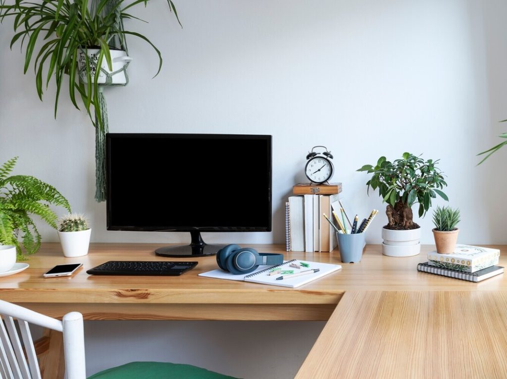 Blank screen of monitor in computer on wooden office desk in stylish business room with white wall.