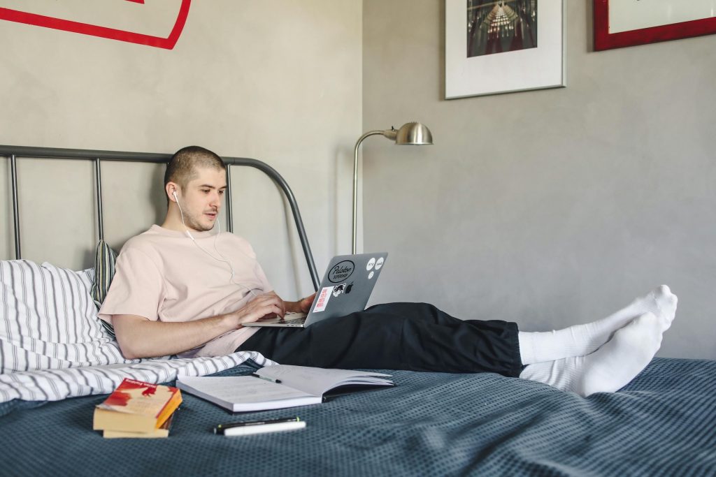 man studying on bed with laptop and books