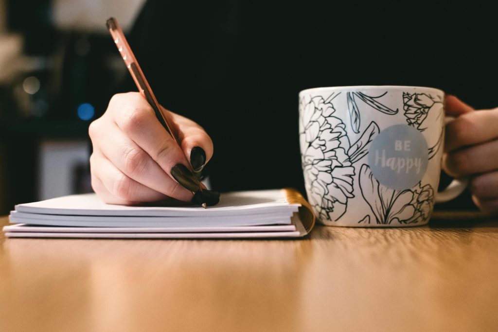 person writing in a notebook and a tea mug