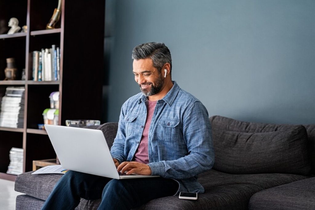 smiling man working on laptop on sofa
