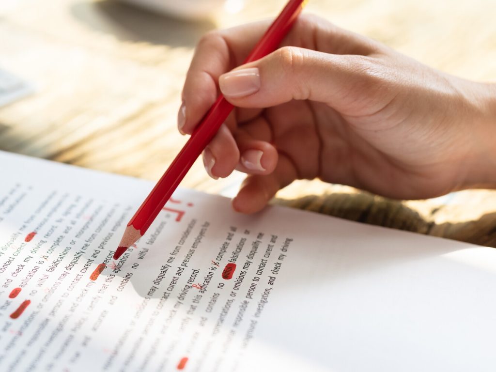 person proofreading papers and marking with  a red pencil