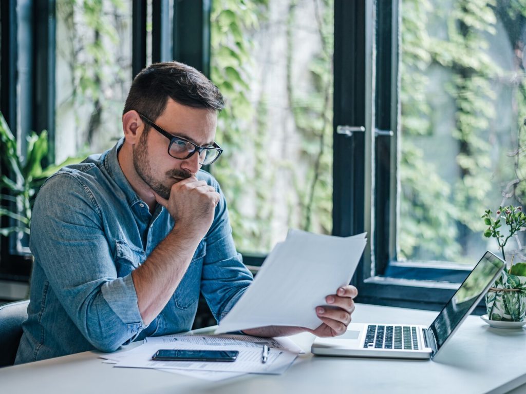 businessman analyzing documents while working on laptop at table