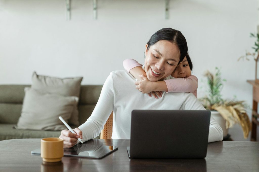 woman working from home with her childs arms around her