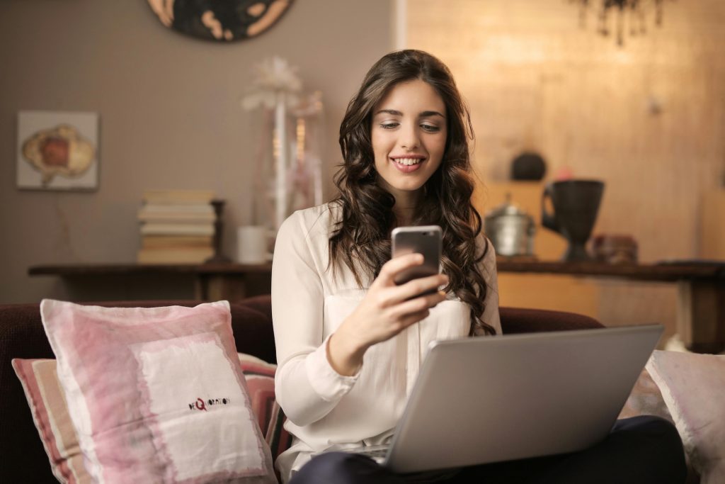woman looking at your phone while working on her laptop on a couch