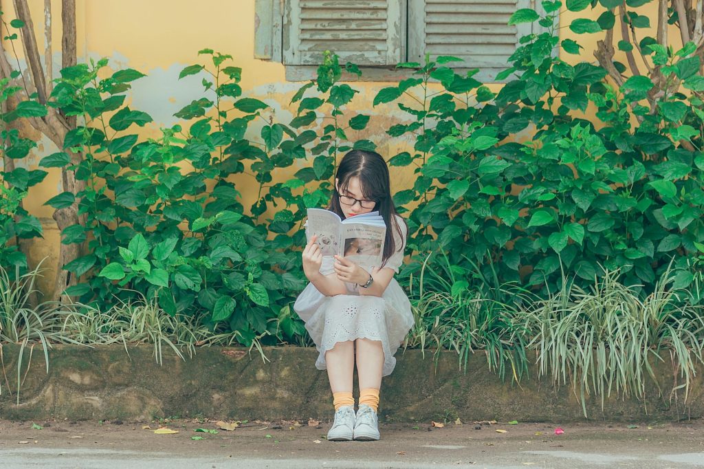 woman sitting on the pavement reading with plants