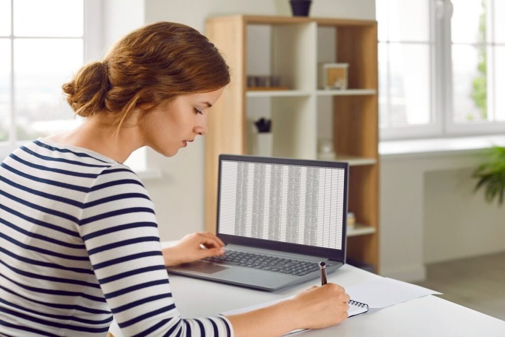 woman taking notes on a pad from a spreadsheet on a laptop
